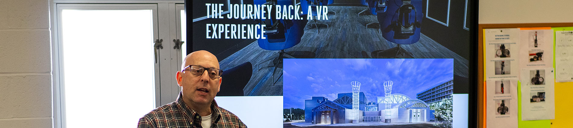 Alan Marcus stands in front of a projector screen that reads The Journey Back: A VR Experience.