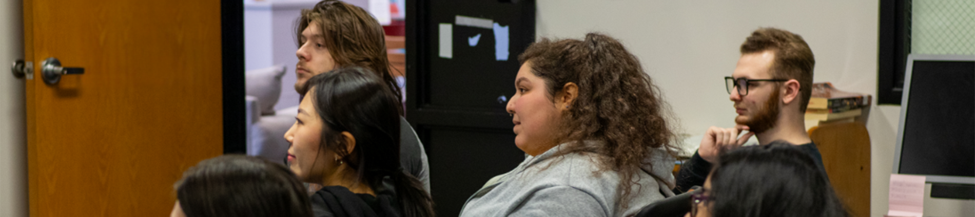 Six high school students sit in a classroom and look at something outside the frame.