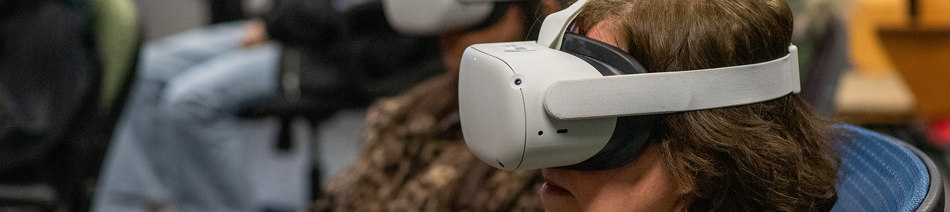 A person sits in a room wearing a VR headset. Others do the same in the background.